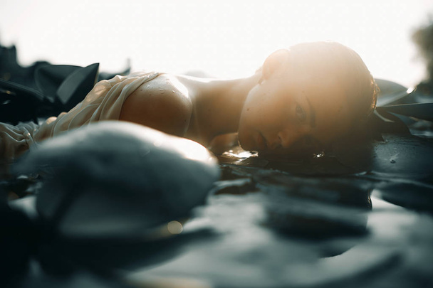 Jonge vrouw liggend in het water onder de bladeren van waterlelie. - Foto, afbeelding