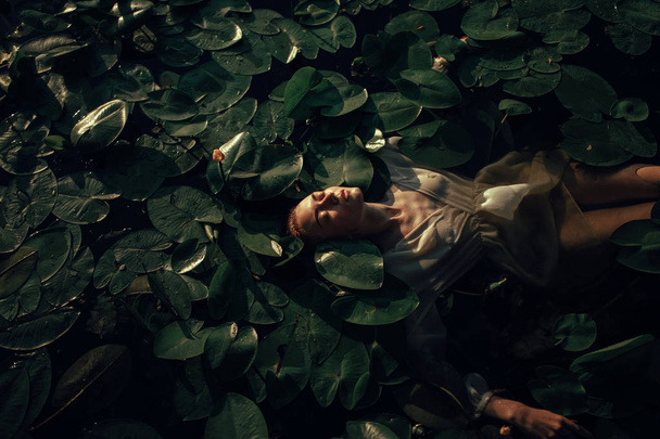 Mujer joven yaciendo en el agua entre las hojas y flores de y
 - Foto, Imagen