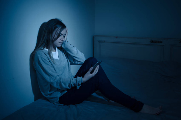 Young teenager girl suffering mobile cell phone addiction feeling lonely and depressed having insomnia needing to be connected sitting on bed late at night. In - Photo, image