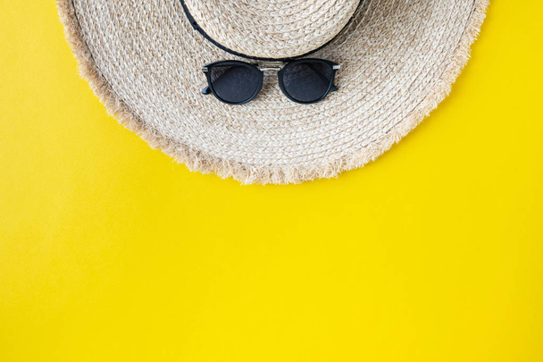 Stylish wicker straw hat with sunglasses on bright yellow background - Foto, afbeelding