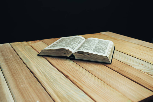 Offenes Bibelbuch auf Holztisch und schwarzem Hintergrund. - Foto, Bild