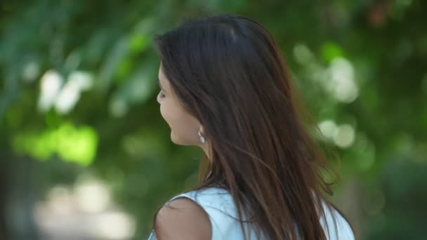 Gorgeous girl smiling and turning her head around playfully in summer in slo-mo         Wonderful view of a happy brunette girl with long loose hair smiling cheerily and turning her head around in an effective way in a park in summer in slo-mo - Footage, Video