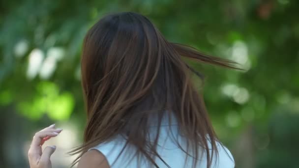 Beautiful girl smartening up and turning her head around with a smile in slo-mo         Gorgeous view of a cheerful brunette girl with long loose hair smartening up and turning her head around with a frolicking smile in a park in summer in slo-mo - Felvétel, videó