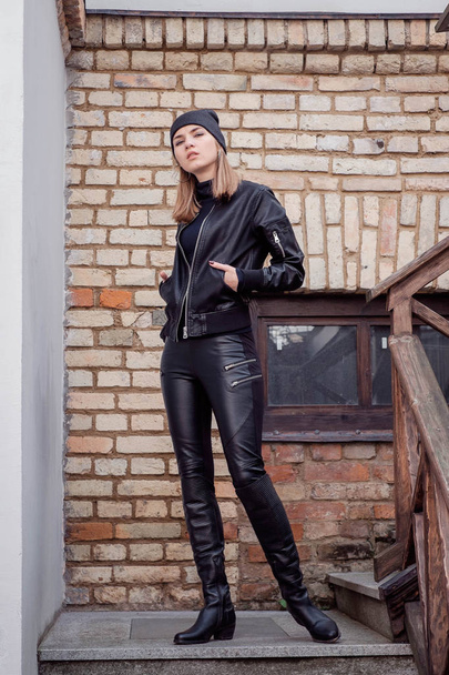 stylish beautiful girl woman blonde posing walks through the city street style in a black hat, black leather jacket and pants, high boots. Portrait. sitting on the steps. - Фото, зображення