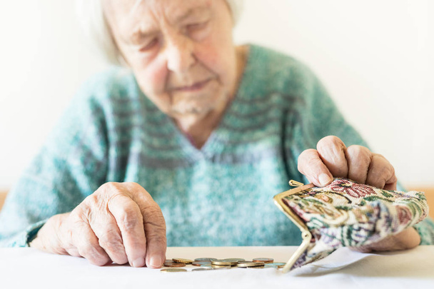 Concerned elderly woman sitting at the table counting money in her wallet. - Фото, зображення
