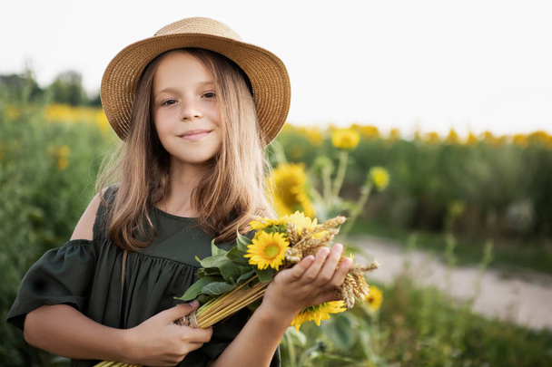Little girl blogger in sunflowers. In a hat and a beautiful dress. With a vintage camera. - Fotó, kép