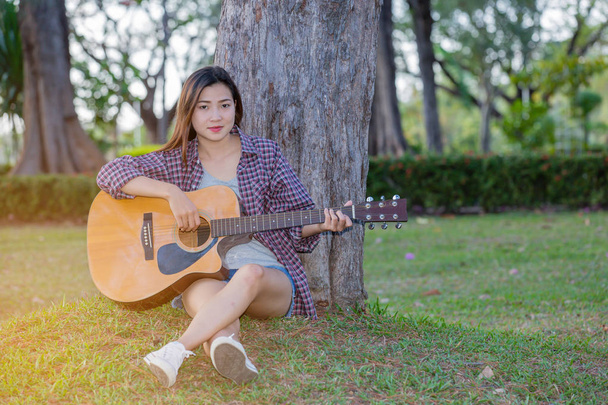 Молода азіатська дівчина в лісі з гітарою в саду
 - Фото, зображення