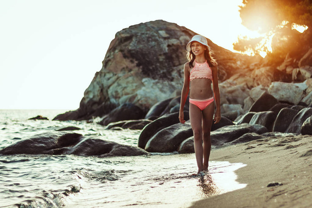 Ευτυχισμένος έφηβος κορίτσι χαλαρωτικό σε βραχώδης παραλία στο ηλιοβασίλεμα - Φωτογραφία, εικόνα