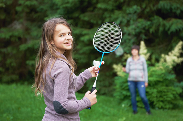 Lächelndes Teenager-Mädchen beim Badminton mit ihrer Mutter im Freien - Foto, Bild