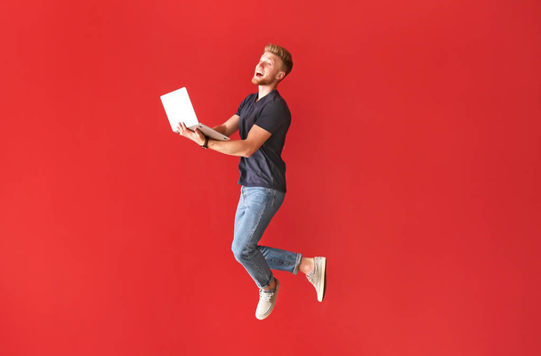 Jumping junger Mann mit Laptop auf farbigem Hintergrund - Foto, Bild