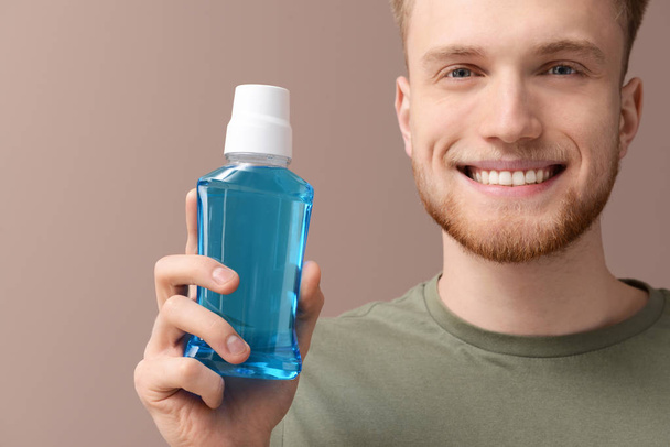 Young man with bottle of mouthwash on color background - Zdjęcie, obraz