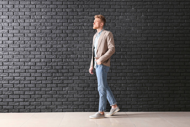 Μοντέρνος νέος άντρας κοντά στο σκοτεινό τοίχο τούβλων - Φωτογραφία, εικόνα