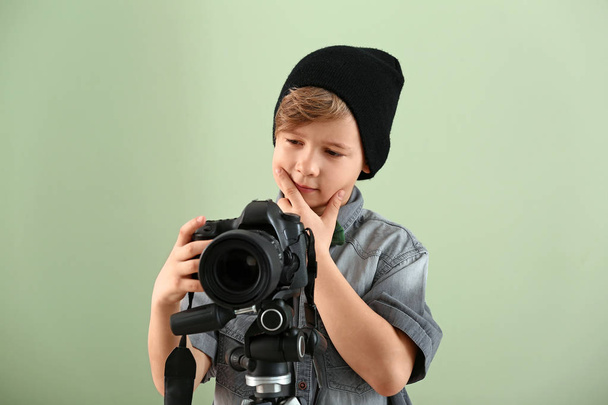 Thoughtful little photographer with professional camera on color background - 写真・画像