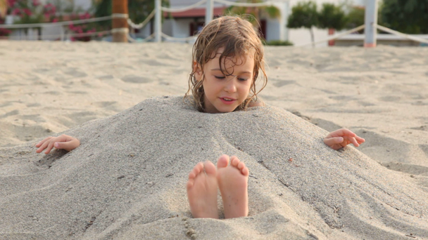 Menina sorri sentado cheio de areia no pescoço na praia
 - Filmagem, Vídeo