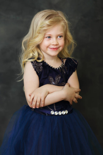 beautiful smiling little girl over dark background look outside the picture - Foto, Imagem