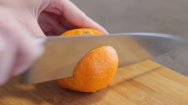 Caucasian girl in the kitchen. Cut the orange into round slices. Girl cuts an orange fruit with a metal knife on a wooden board. Juice dripping down the fruit. Cooking food. - Video, Çekim