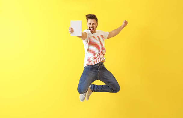 Jumping young man with book on color background - Fotoğraf, Görsel