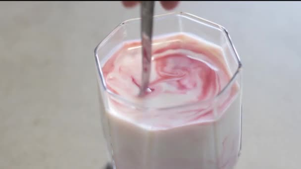 Transparent glass cup with milk on the table. Red circles on a white surface. Stir the red liquid in the glass a metal teaspoon to get a pink color. Healthy, sweet drink. Berry syrup. - Video, Çekim