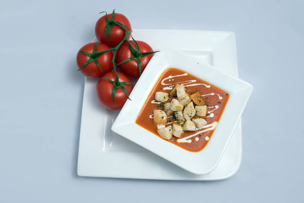 un Golpe de héroe de una sopa de tomate con migas de pan, orégano sobre un fondo blanco mínimo con un ángulo diagonal 45
 - Foto, imagen