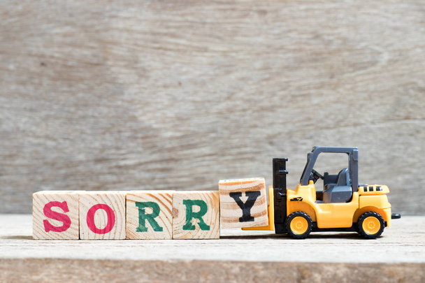 Spielzeug Gabelstapler halten Buchstabenblock y zu vervollständigen Wort sorry auf Holz Hintergrund - Foto, Bild