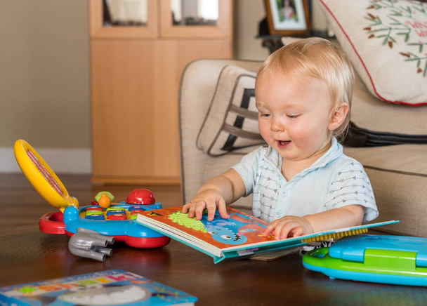 Infant caucasian boy reading book rather than using computer - Photo, Image