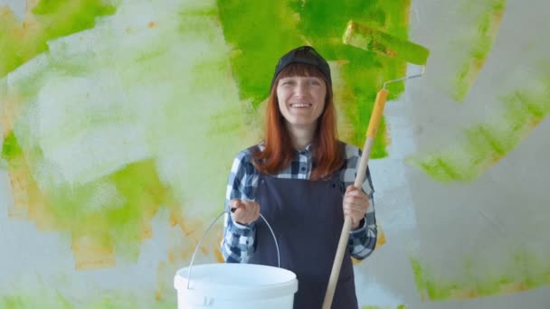 Una joven hace reparaciones. La chica del rodillo pinta las paredes. La chica hace reparaciones y sonríe. Pintando las paredes de la casa. Construcción y reparación. Trabajos de reparación
 - Imágenes, Vídeo