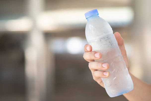 primo piano giovane mano tenendo fresco bottiglia di acqua potabile fredda da una plastica all'aperto
. - Foto, immagini