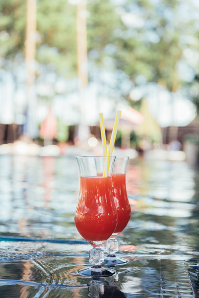 two glasses with tasty, natural fruit beverage at poolside - Photo, image