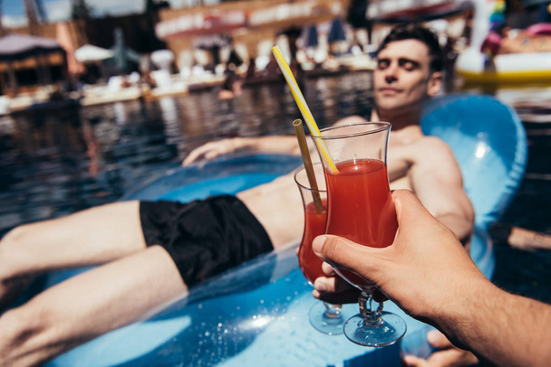 abgeschnittene Ansicht von Männern, die beim Entspannen in der Nähe des Swimmingpools Gläser mit Erfrischungsgetränken klirren - Foto, Bild