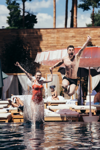 Aufgeregtes junges Paar hält Händchen beim Sprung in Schwimmbad - Foto, Bild