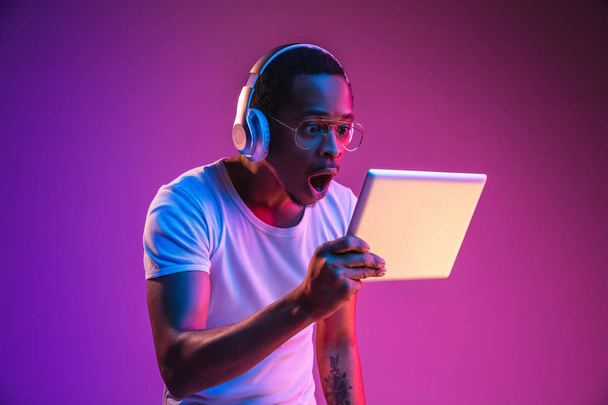 Young african-american mans listening to music in neon light - Foto, imagen