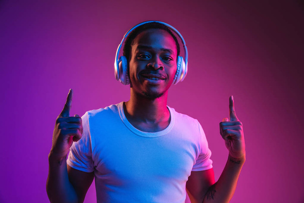 Young african-american mans listening to music in neon light - Zdjęcie, obraz