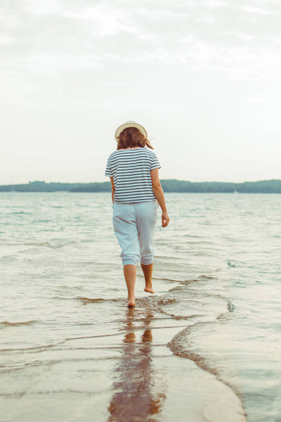 женщина в белой одежде прогуливаясь по морскому пляжу
 - Фото, изображение