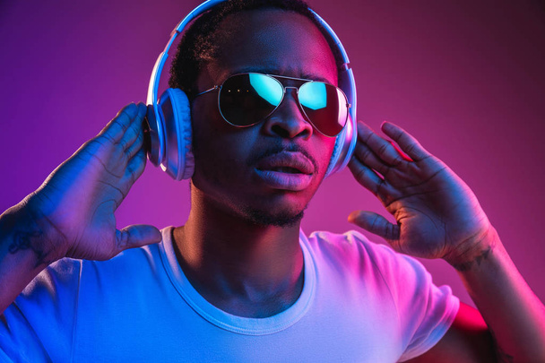 Young african-american mans listening to music in neon light - Foto, immagini