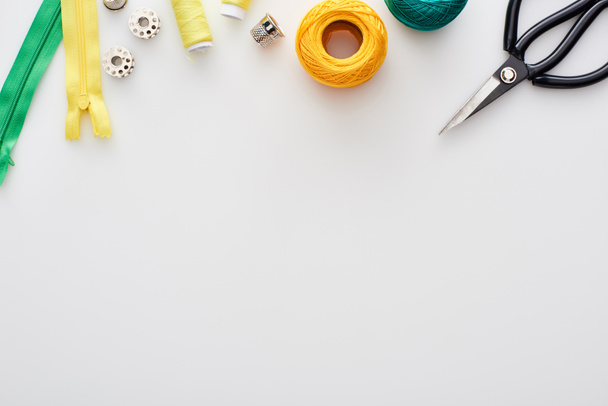 top view of scissors, knitting yarn balls, zippers, threads, thimble and bobbins on white background  - Photo, Image