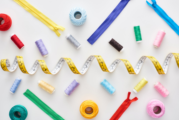 top view of measuring tape, colorful threads and zippers on white background  - Foto, afbeelding