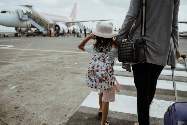 little girl and mother holding hands walk towards the plane - Photo, Image