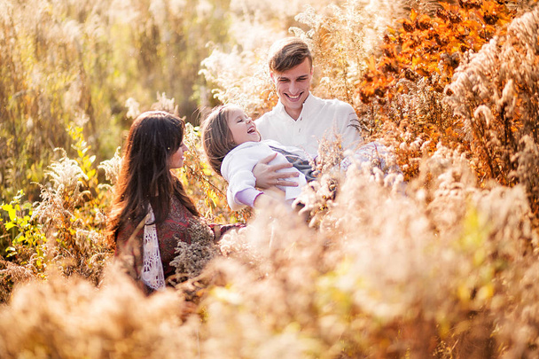Famille heureuse posant parmi les plantes sèches jaunes d'automne
 - Photo, image