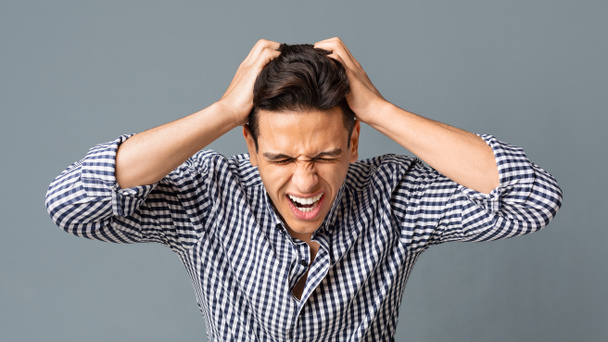 Frustrovaný mladý muž tahání jeho vlasy na šedém pozadí - Fotografie, Obrázek
