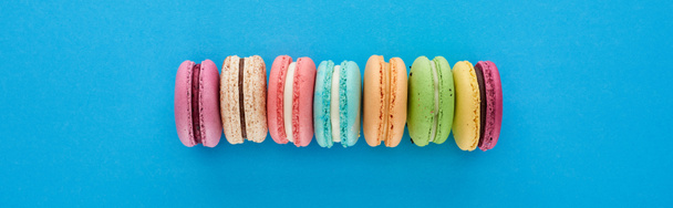 Panoramaaufnahme von bunten köstlichen französischen Makronen in Reihe auf blauem Hintergrund mit Kopierraum - Foto, Bild