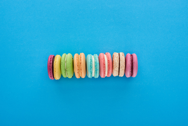 top view of multicolored delicious French macaroons in line on blue bright background - Photo, Image