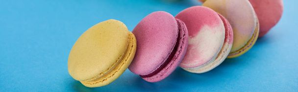 close up view of multicolored delicious French macaroons on blue bright background, panoramic shot - Foto, afbeelding