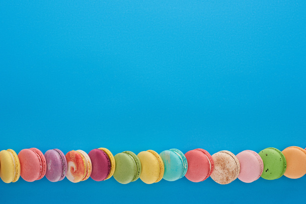 line of multicolored delicious French macaroons on blue bright background with copy space - Photo, Image