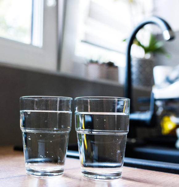 zwei Gläser Wasser in der Küche, mit Leitungswasser und zwei Flaschen Mineralwasser. geringe Schärfentiefe. Wasserknappheitskonzept, Wassersparen. Körperhydratation mit sauberem & klarem Wasser. - Foto, Bild