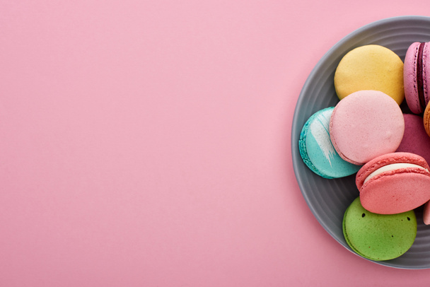 plate with multicolored delicious French macaroons on pink background with copy space - Foto, imagen