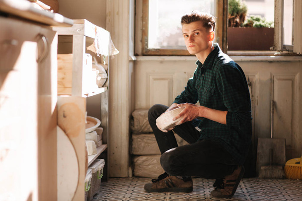 Чоловік-гончар шукає посуд для роботи. Молодий чоловік гончар у своїй майстерні. Красивий чоловік працює
 - Фото, зображення