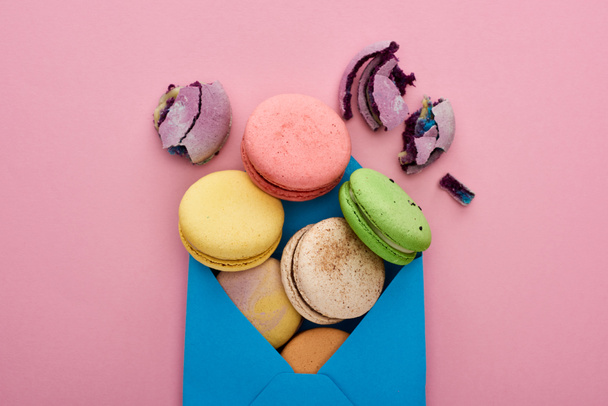top view of multicolored delicious French macaroons in blue postal envelope on pink background - Foto, afbeelding