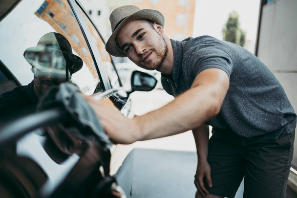 Young handsome man with hat cleaning car with rag, car detailing (or valeting) concept.  - Foto, Bild