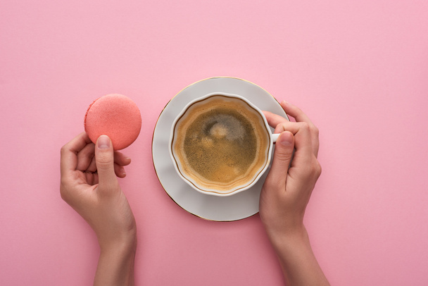 partial view of woman drinking coffee with delicious French macaroon on pink background - Fotoğraf, Görsel