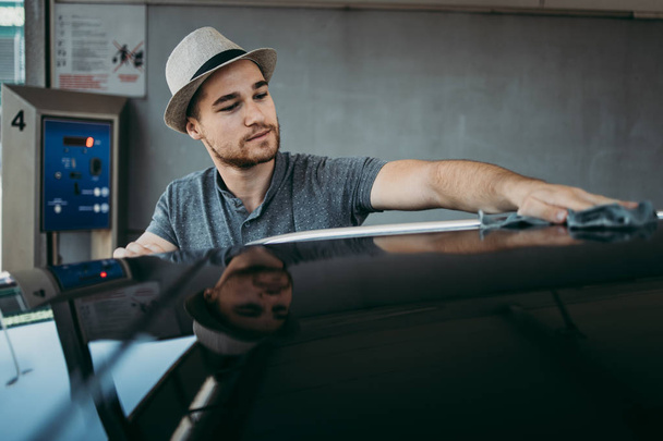 Young handsome man with hat cleaning car with rag, car detailing (or valeting) concept.  - Foto, afbeelding